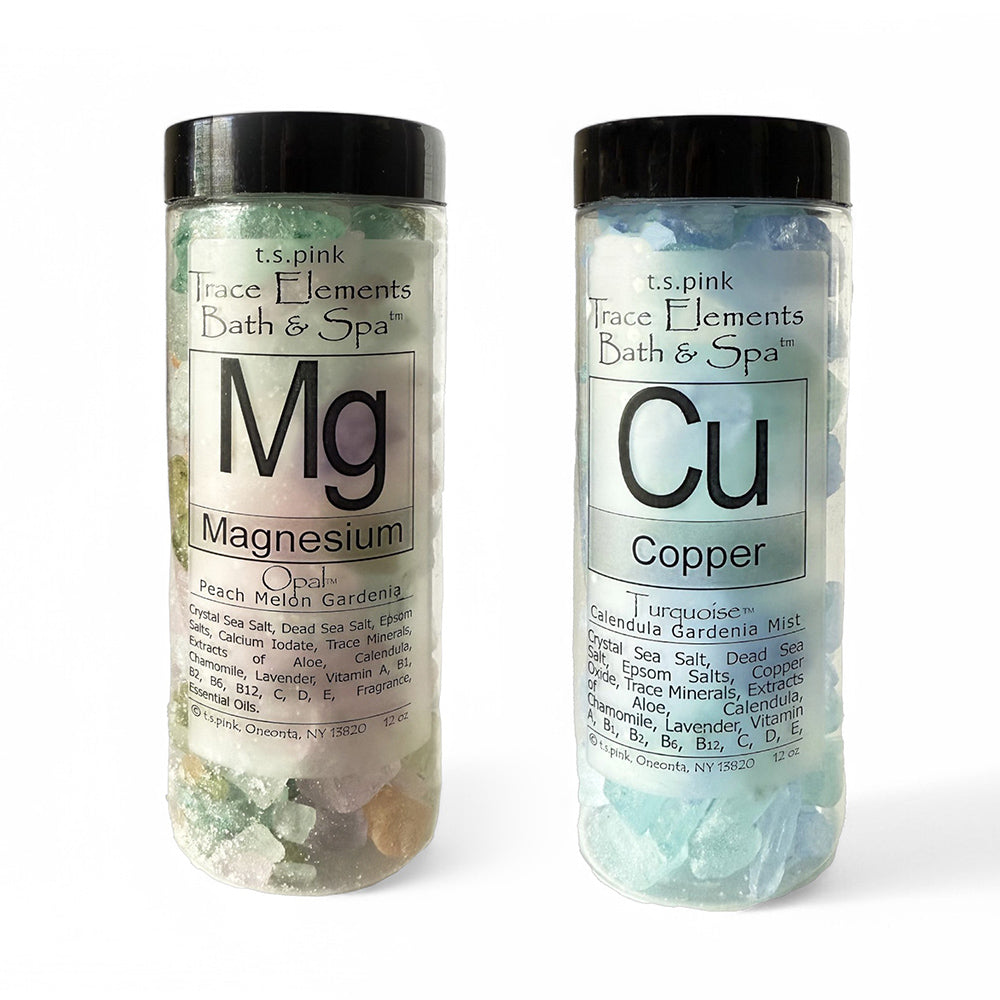 Image of a high-end bath salt duo, including "Magnesium Bath Salts" and "Copper Bath Salts," elegantly packaged in clear jars with black lids. The salts' textures and rich minerals are beautifully displayed, complementing the luxurious, spa-like aesthetic.