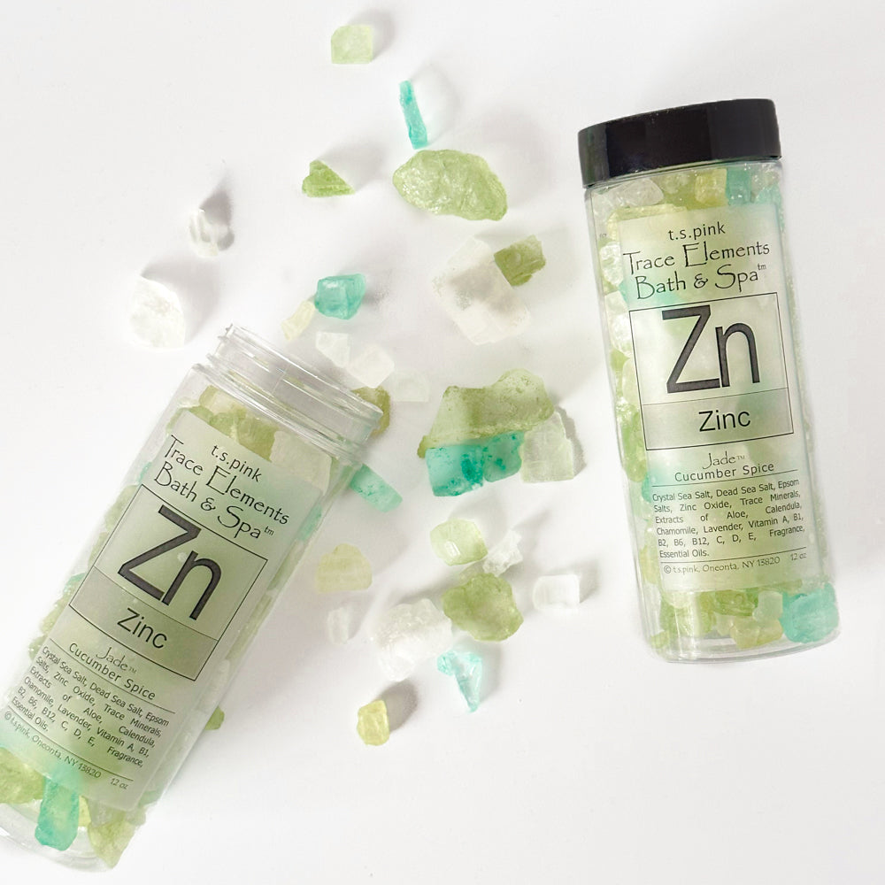 A tipped-over jars of Rengöra colorful bath salts in shades of green, white, and turquoise spills onto a white surface.