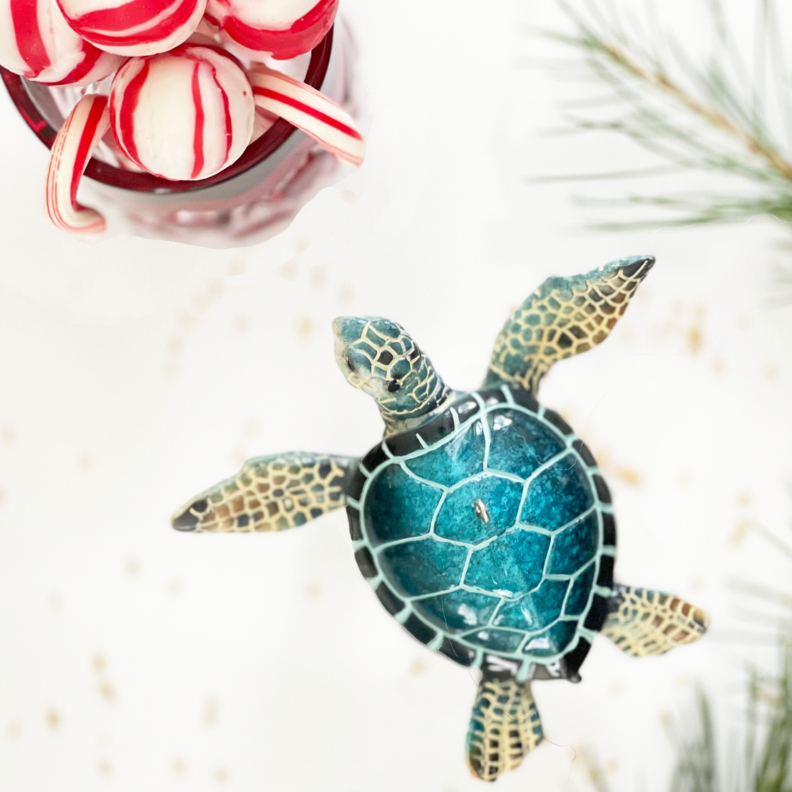 rengöra's blue sea turtle ornament shown swimming towards peppermint candies with a pine bough in the background