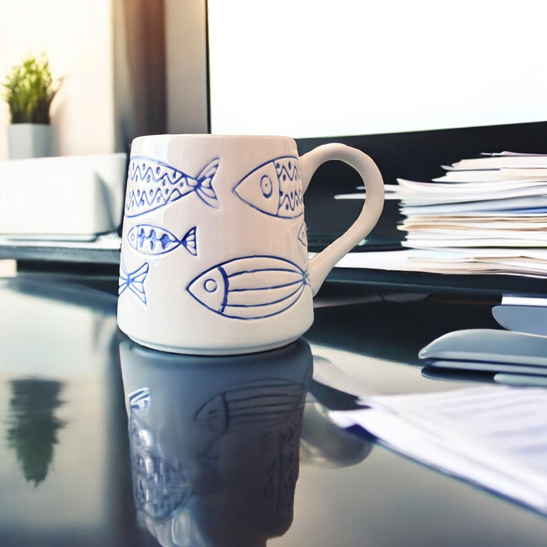 Ceramic rengöra fish mug on a sleek office desk beside stacked papers and a computer monitor — blending coastal charm into a modern workspace.