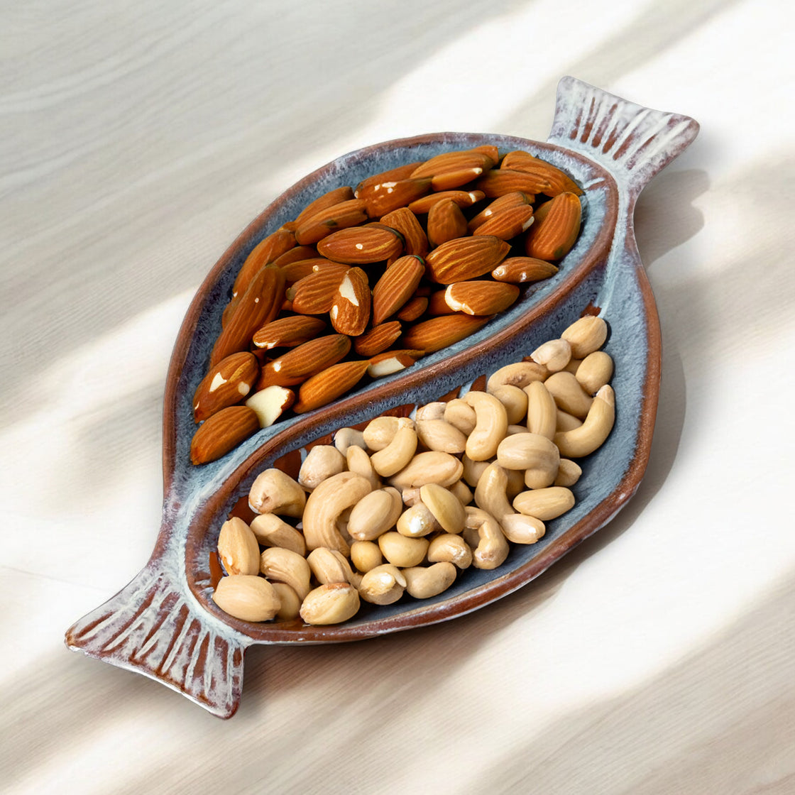 Ceramic dual fish-shaped serving dish filled with almonds and cashews, perfect for snacks.