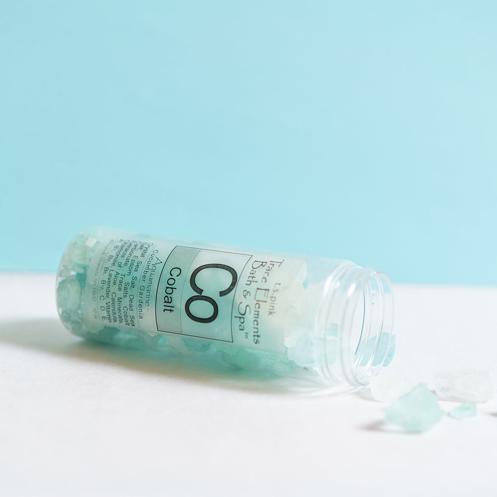 Cobalt bath crystals / bath salts laying on a counter spewing out of the container with an aqua blue background wall.