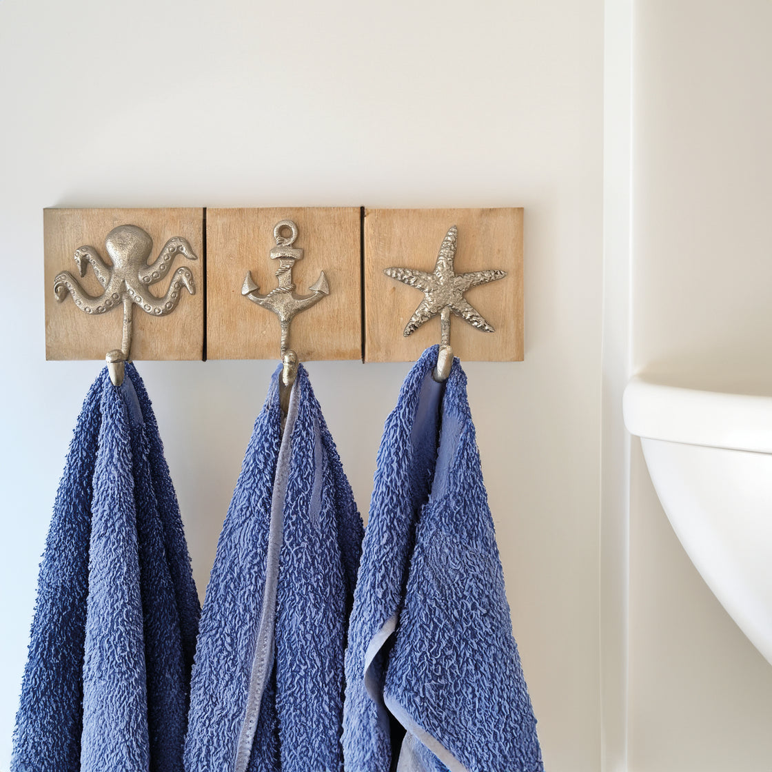 Three nautical hooks mounted on a wall, each holding a vibrant blue towel, styled in a crisp, clean bathroom space.