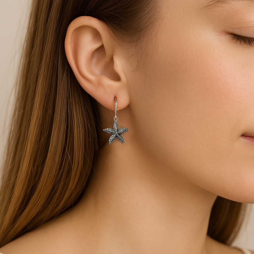 Close-up of a woman's ear adorned with a silver starfish-shaped earring, shown against a soft, neutral background.