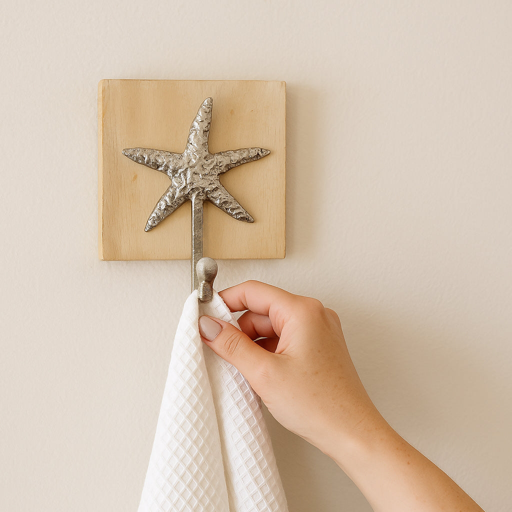 Close-up of a starfish wall hook with a hand hanging a white towel.