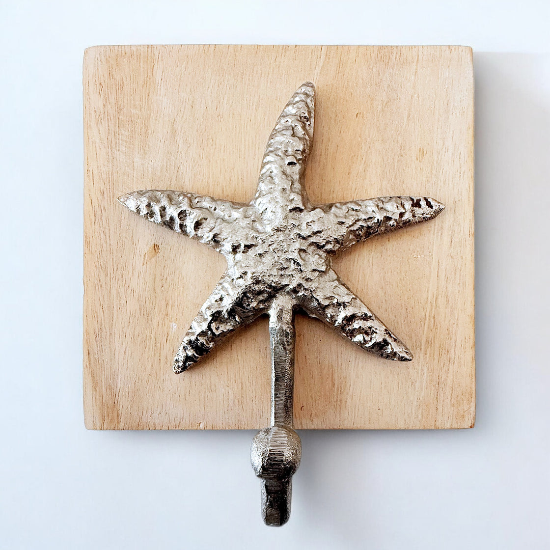 Close-up of a single metal starfish wall hook mounted on natural wood.