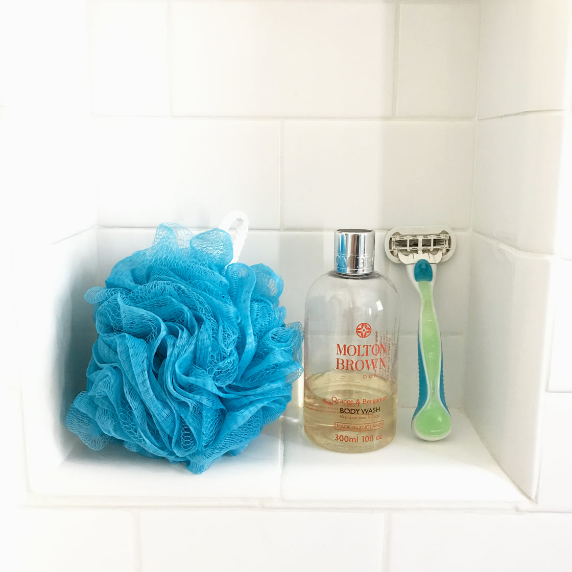 The rengora mesh scrubber placed alongside a bottle of body wash and a shaver within a bathroom setting