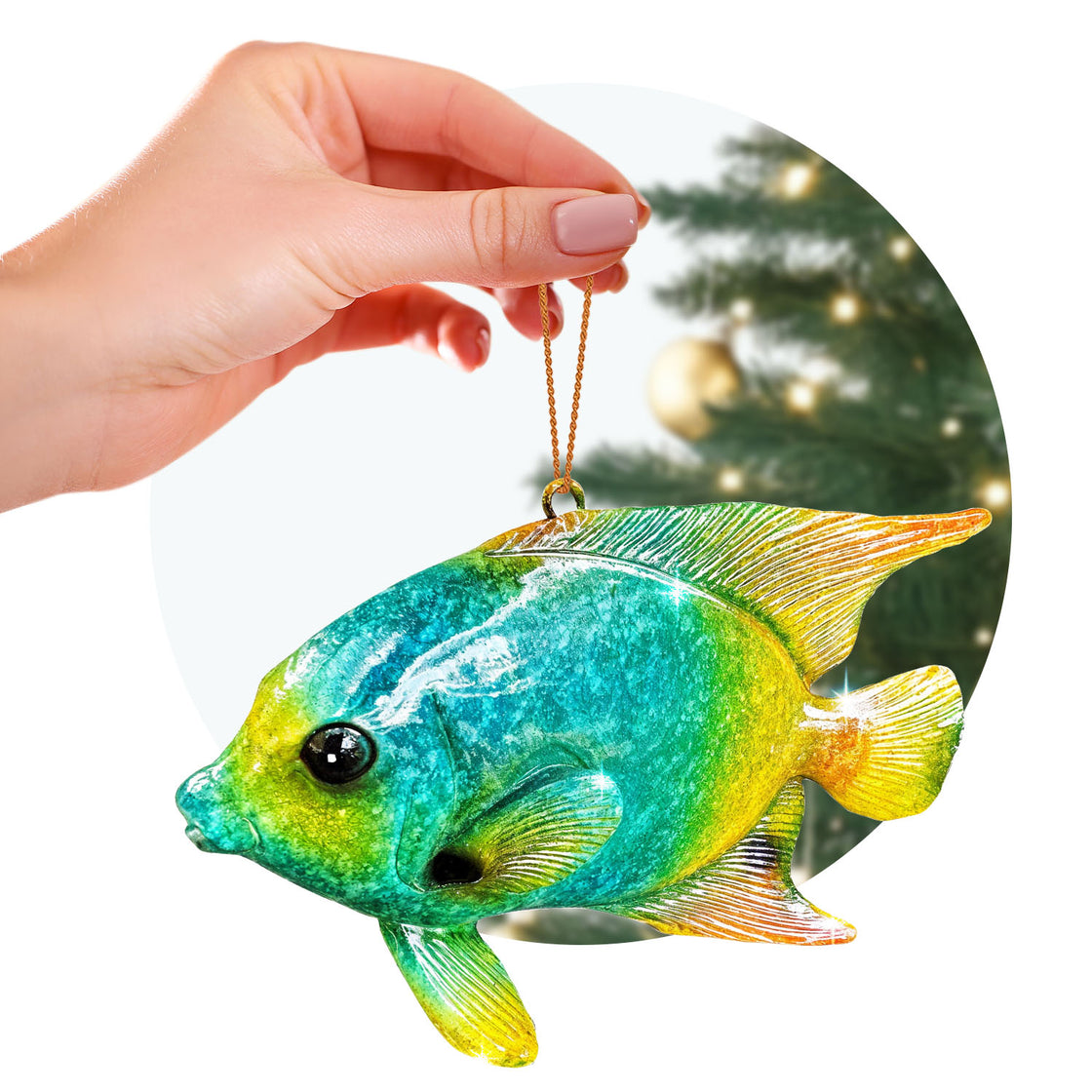 A hand holds a brightly colored tropical fish ornament by its gold loop. The fish has a gradient of teal, yellow, and orange hues, with a finely detailed texture, and is shown against a softly glowing Christmas tree background.