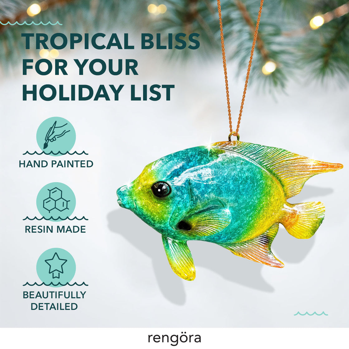 A close-up of the tropical fish ornament, showcasing its gradient blue and yellow coloring and detailed fins. It hangs from a gold cord, with soft pine branches and warm holiday lights blurred in the background