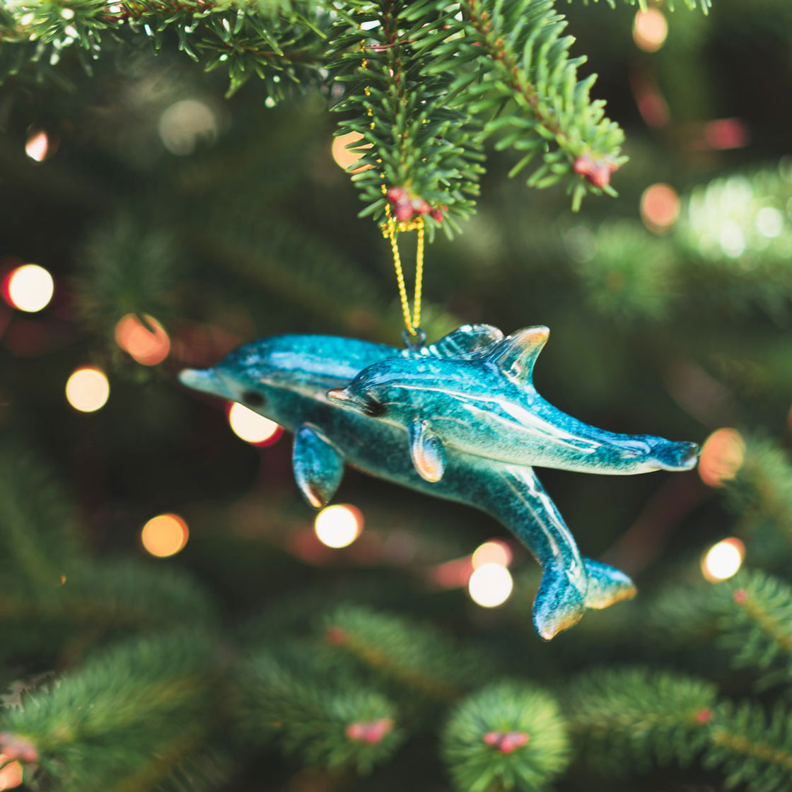 ceramic blue dolphins Christmas tree ornament hanging elegantly on a green Christmas tree with white lights in the background