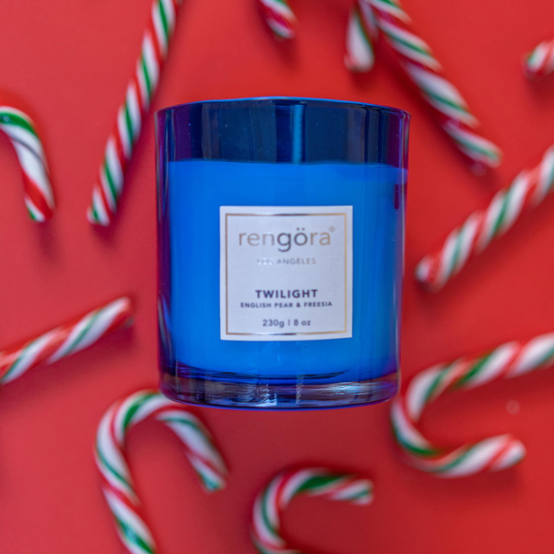 The Rengöra's Twilight-scented home candle set against a festive red Christmas-themed background adorned with Christmas candies