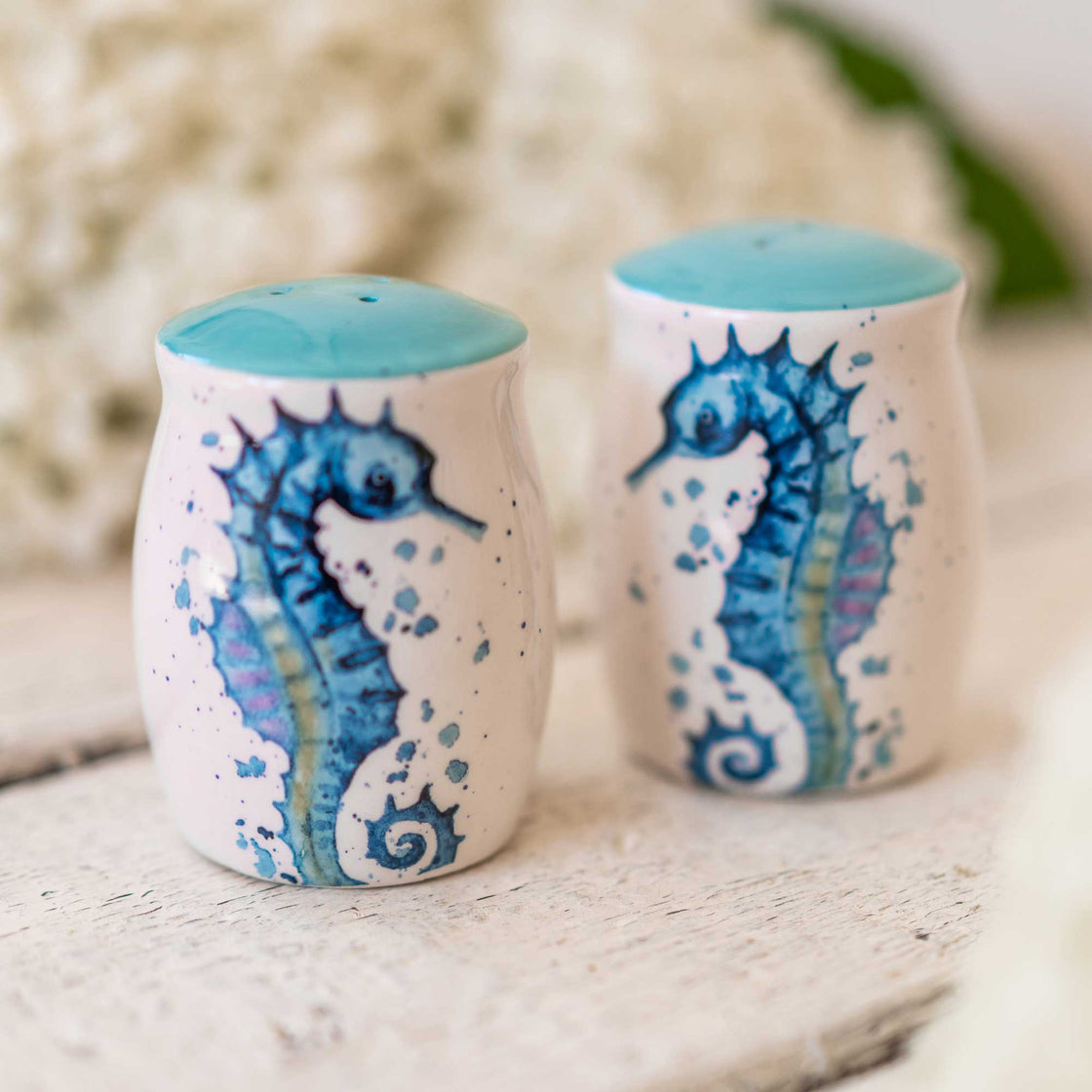 seahorse salt and pepper shakers on a rustic wooden table with white flowers blurred in the background