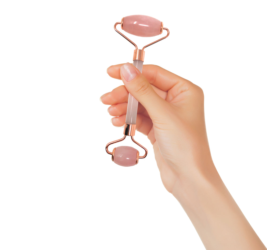 woman's hand holding up a two-sided rose quartz roller with one larger roller on the top for use with cheeks, neck, and forehead - and a smaller roller on the bottom for use on the eyes