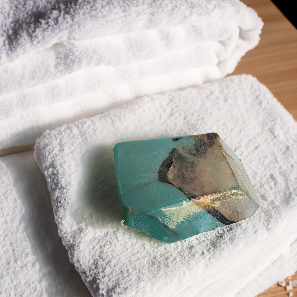 A turquoise blue teal soap nestled within a pristine white towel