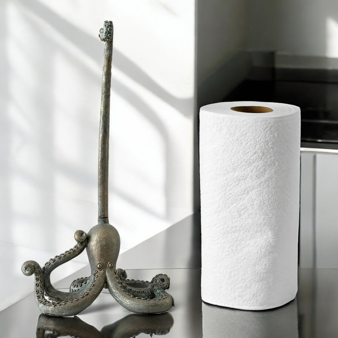 Cast metal octopus paper towel holder next to a roll of paper towels on a sleek kitchen counter with natural light.