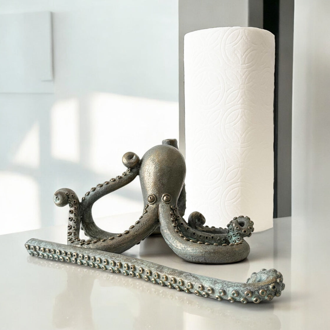 Disassembled octopus paper towel holder beside a roll, showcasing the weighted base and upright tentacle arm.