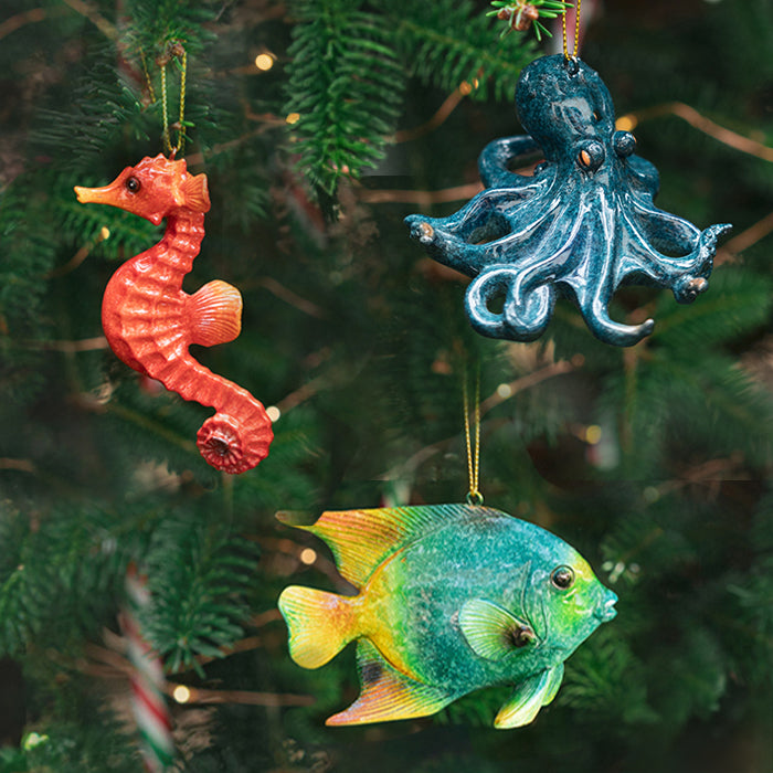 A set of three ocean-inspired Christmas ornaments featuring a seahorse, an octopus, and a tropical fish, all with vibrant colors and intricate details, hanging from a tree.