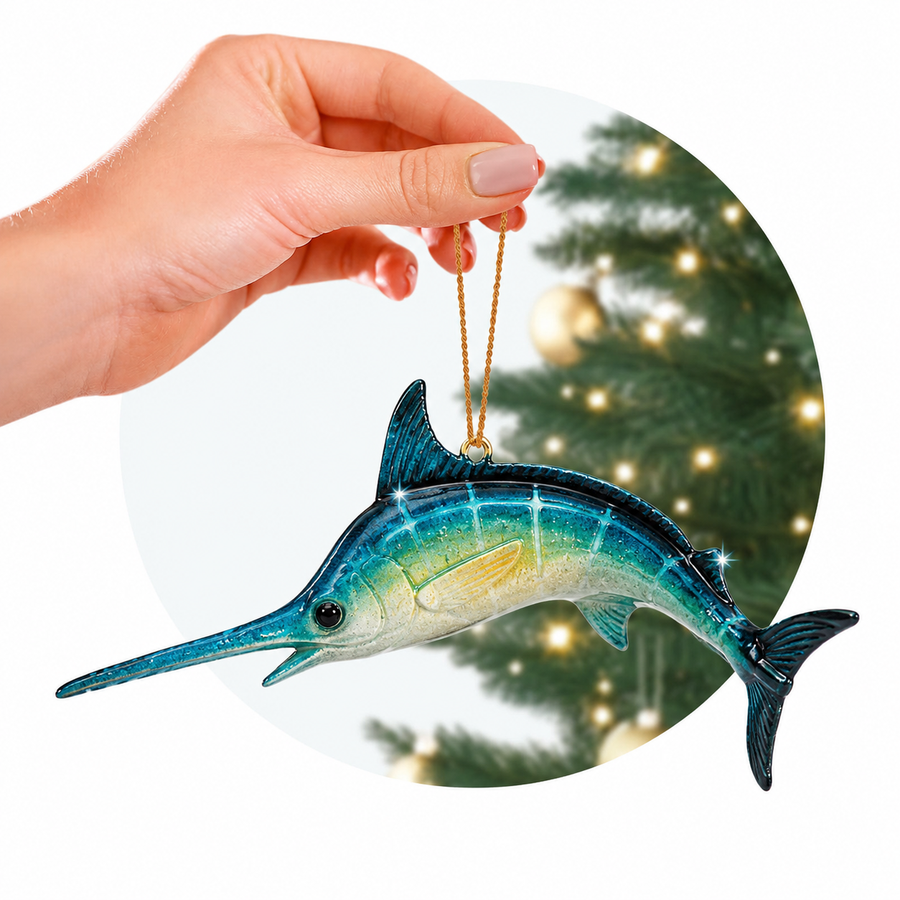 Hand holding a blue and green swordfish ornament with a blurred Christmas tree in the background