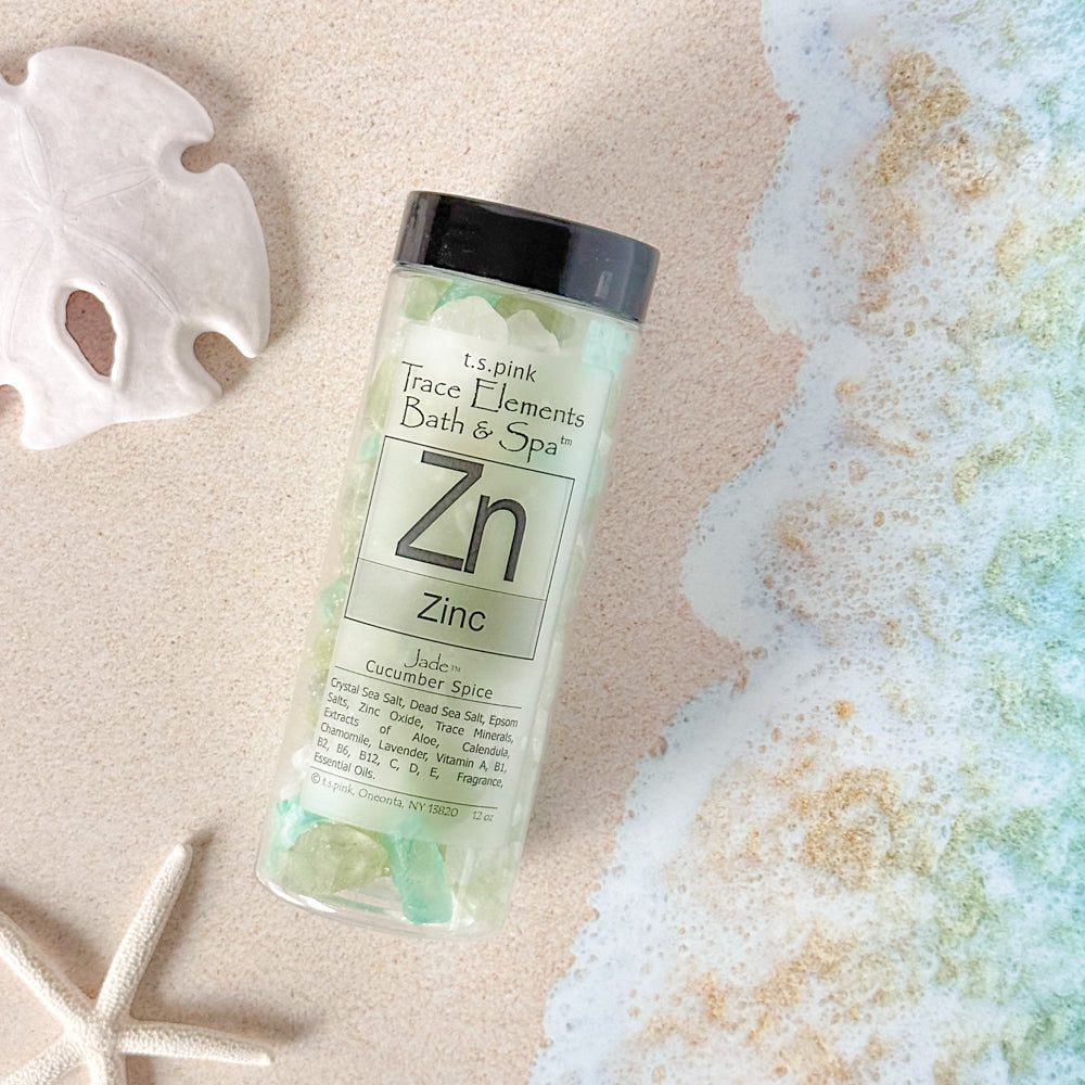 A jar of Rengöra bath salts infused with zinc sits on the sand at the beach, surrounded by natural elements. 