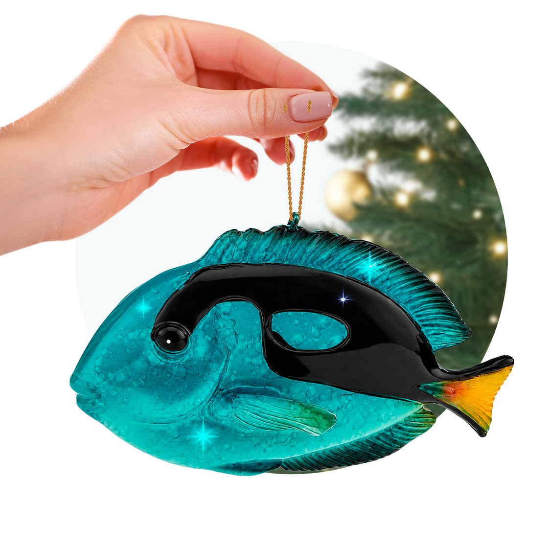 Hand holding a Rengöra tropical blue tang Christmas ornament in front of a softly lit holiday tree.