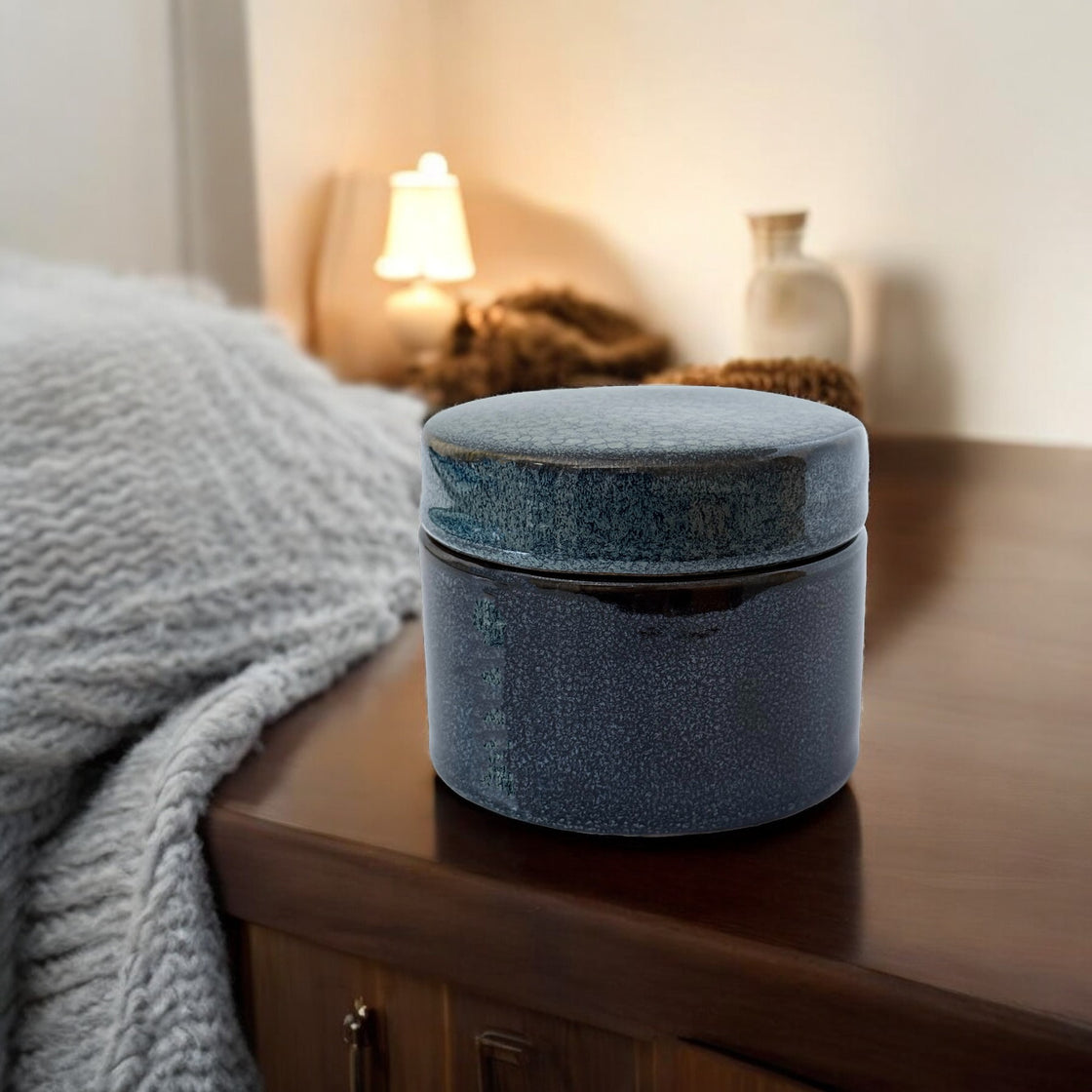 Elegant navy ceramic covered storage container placed on a cozy wooden bedside table in a softly lit bedroom.