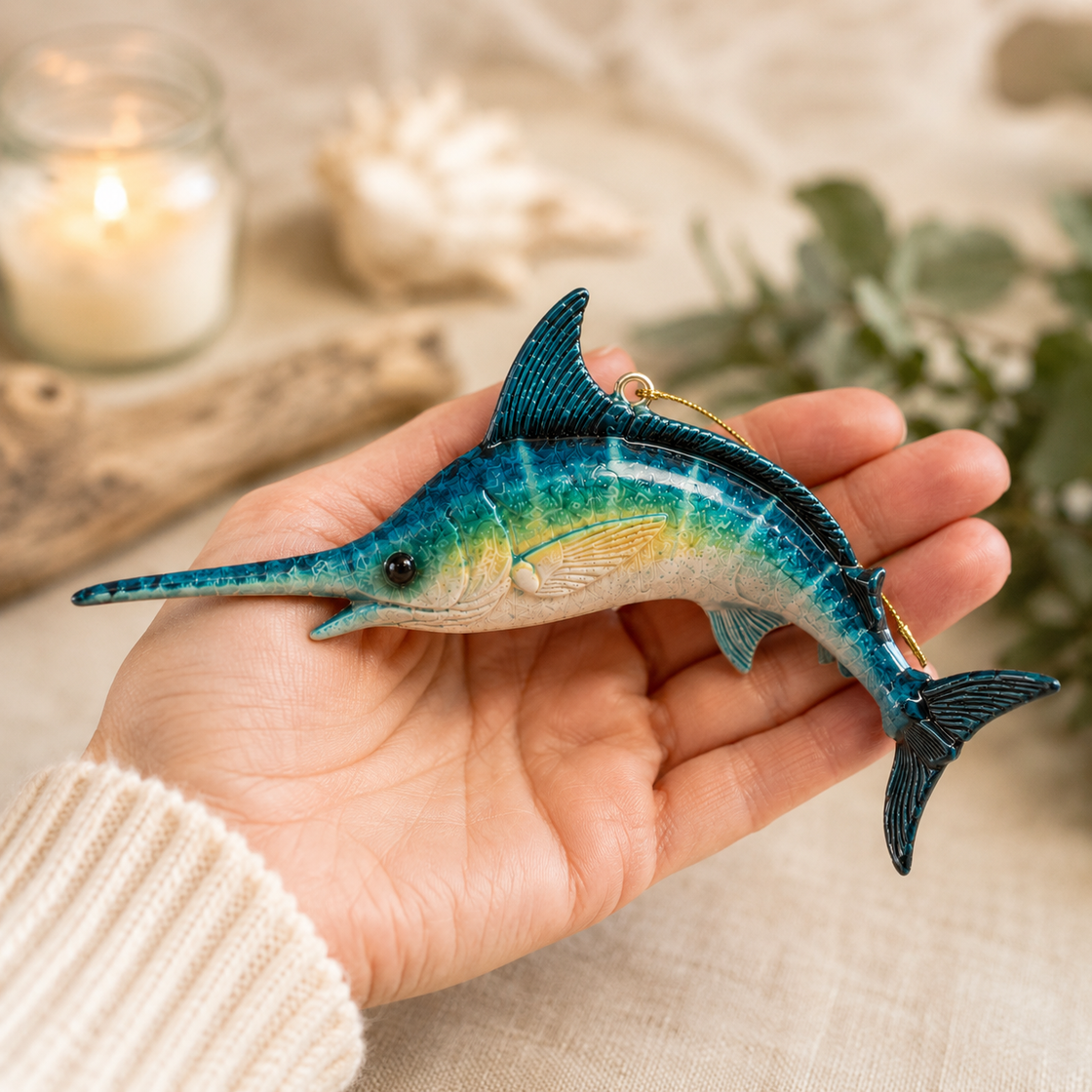 Hand holding a blue and green swordfish ornament with a blurred background