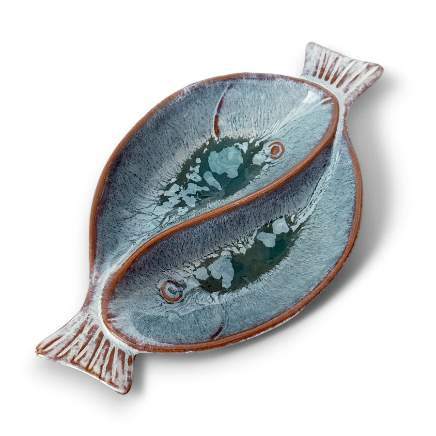 Handcrafted ceramic dual fish-shaped serving bowl with a glossy blue-grey glaze and elegant texture on a white background.