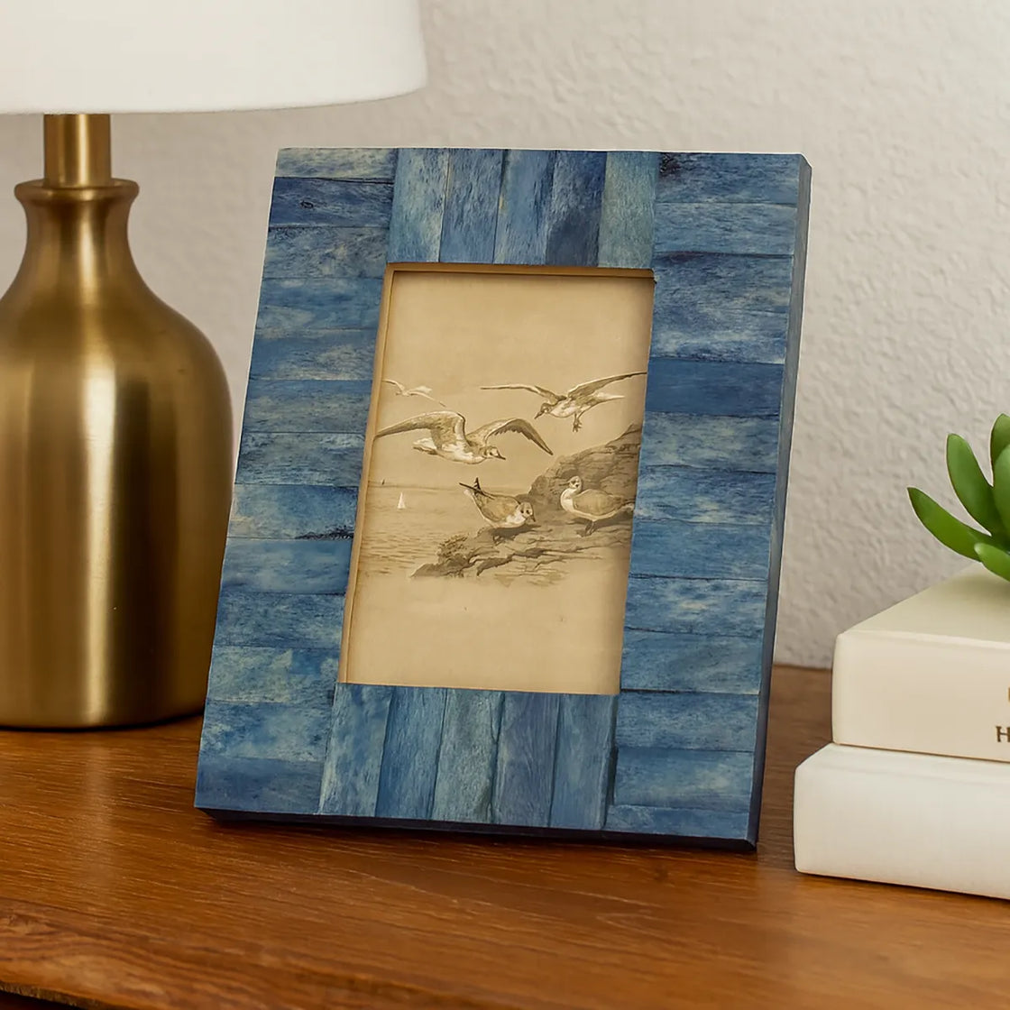 Rengöra handcrafted blue wooden photo frame on bedside table with lamp and books