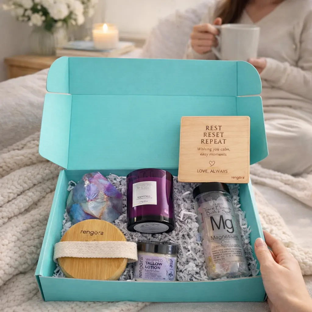 Gift box with self-care items including a candle, lotion, and other products on a bed.