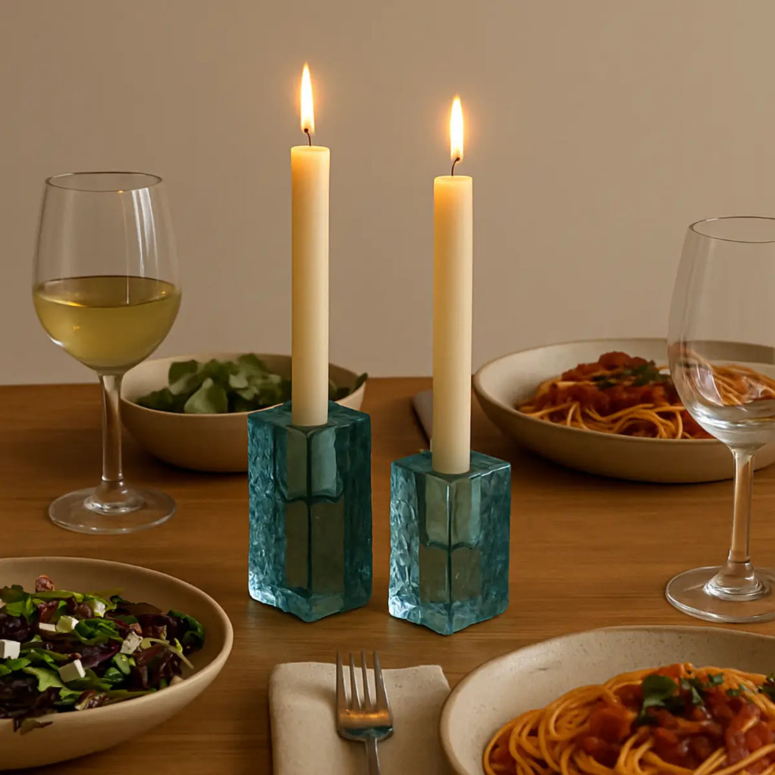Dinner table setting with candles in blue holders, wine glasses, and plates of food.