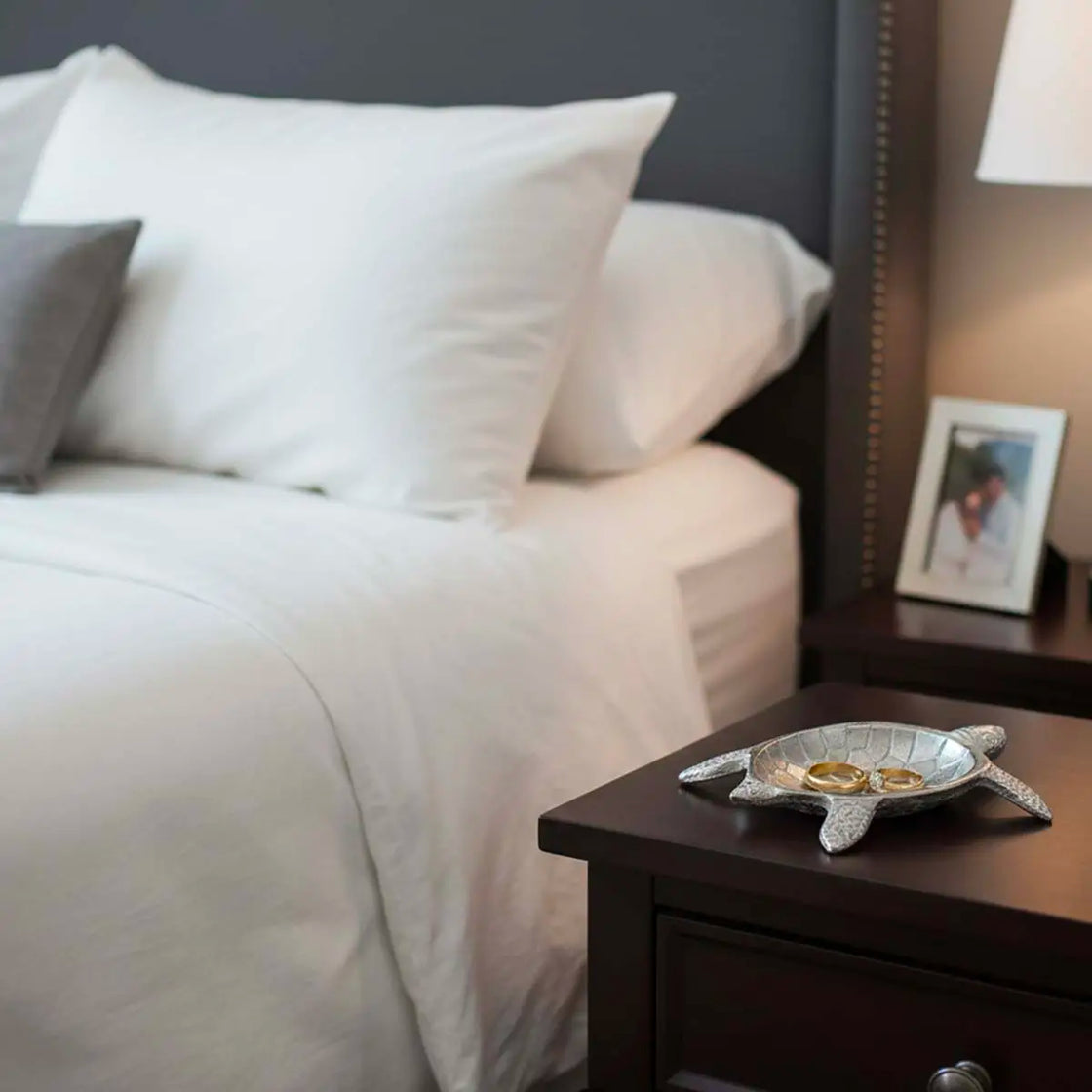 Bedroom with a neatly made bed and a side table with a silver jewelry trinket dish.
