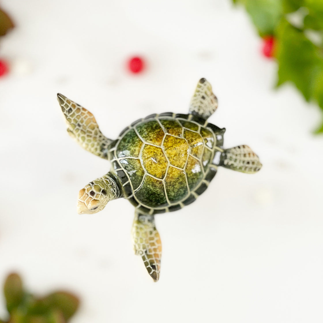 Top view of rengöra's green sea turtle ornament with it's colorful shell floating on a red, white, and green background