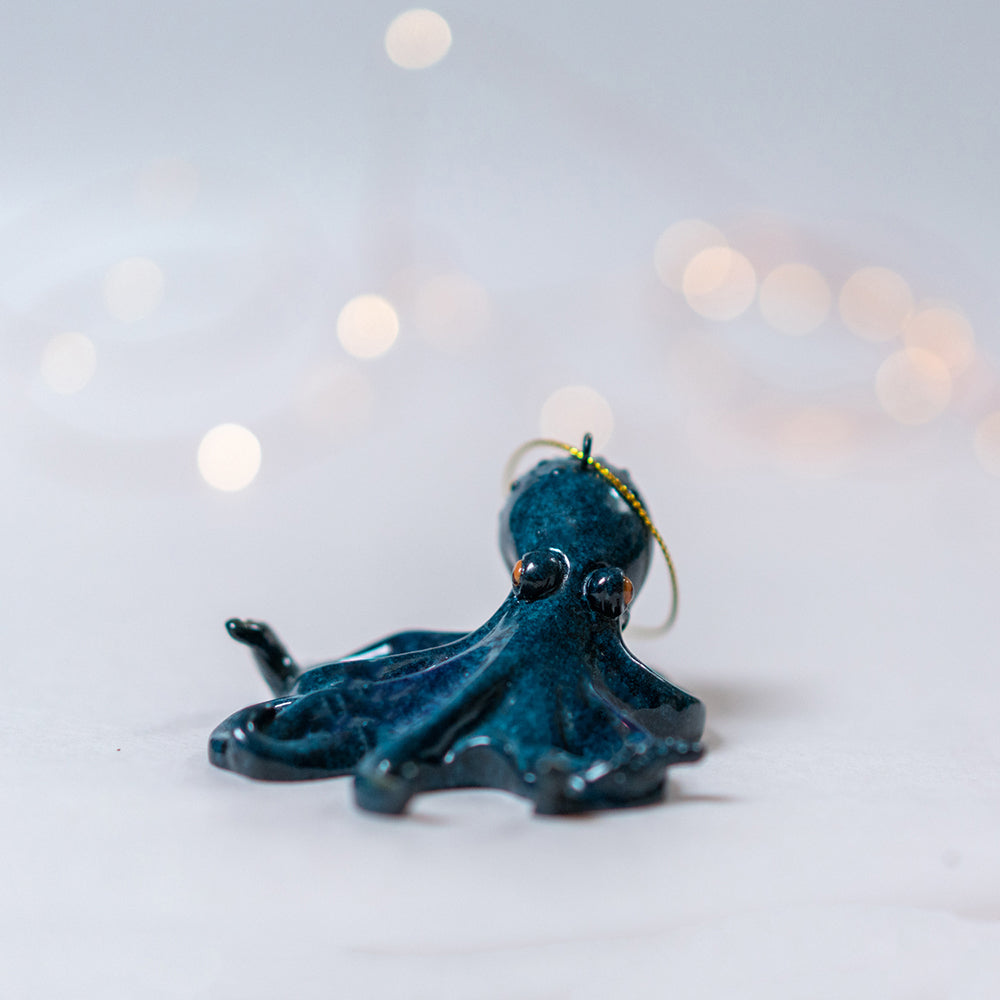 An up-close look at the hand-painted rengora octopus featuring its shiny turquoise blue color set against a softly blurred white background with twinkling Christmas lights