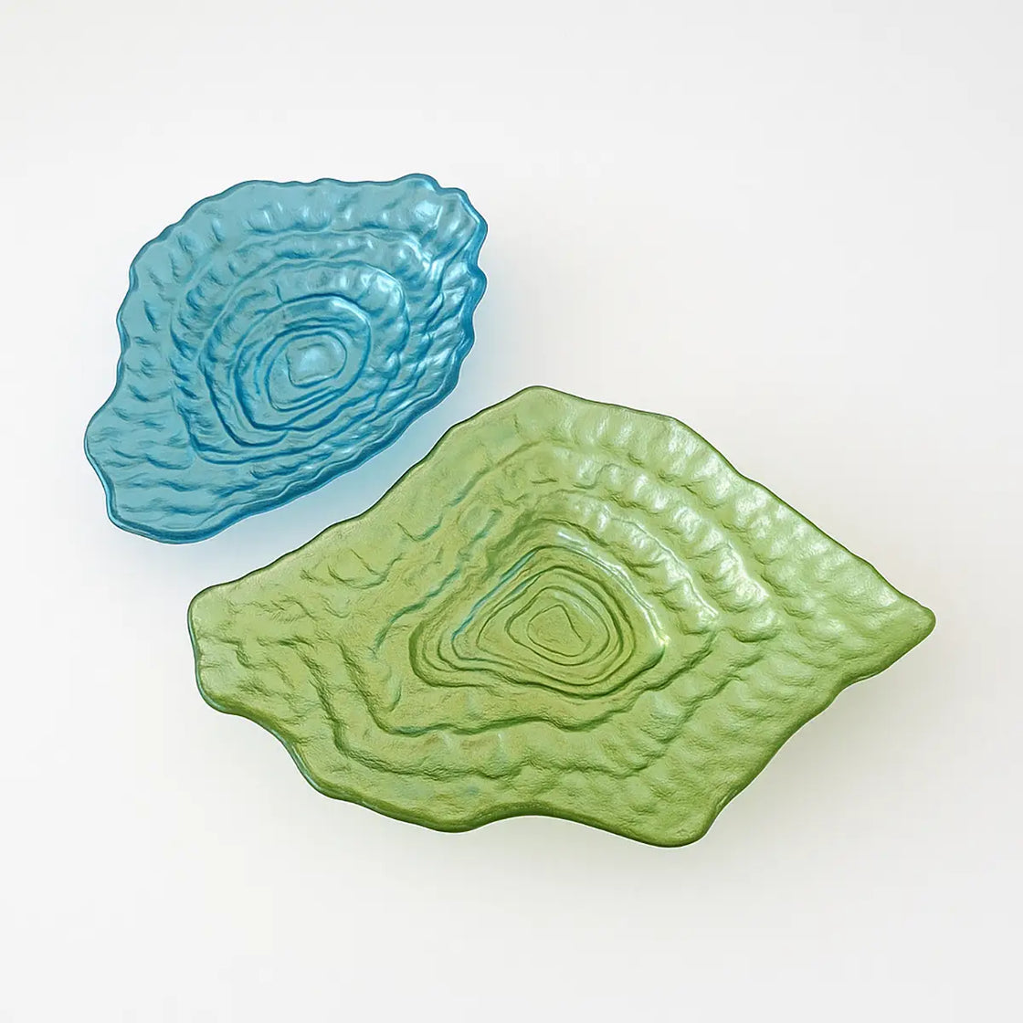 Top-down studio view of blue and green oyster-shaped glass dishes on a white background, showcasing their ripple-like design.