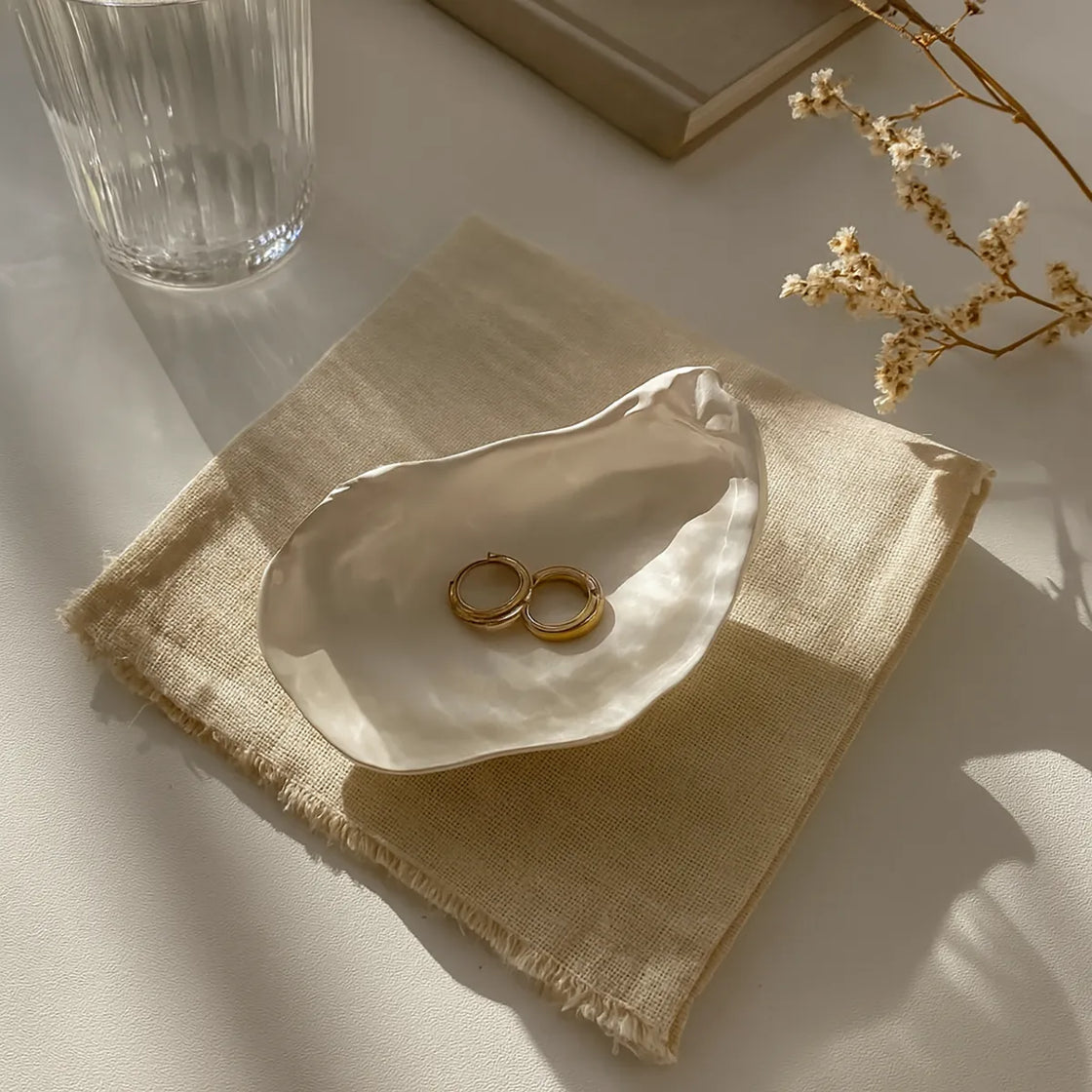 Rengöra ceramic oyster shell jewelry holder with gold earrings in natural light