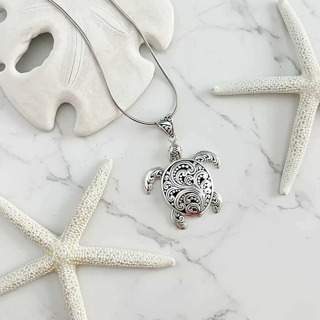 Silver turtle pendant necklace on a marble surface with starfish and sand dollar