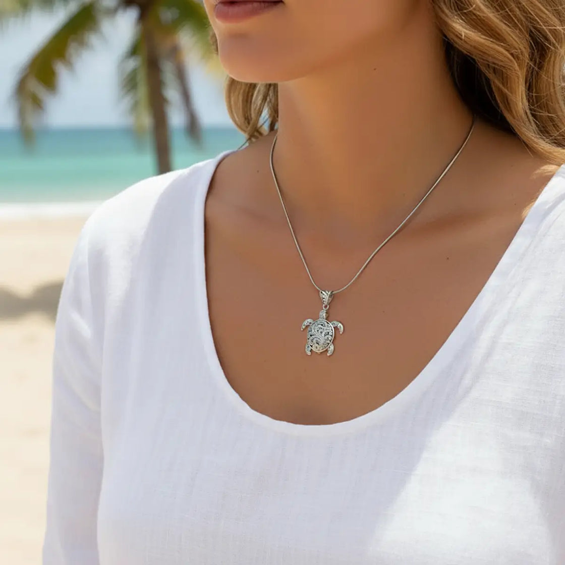 Person wearing a turtle pendant necklace with a beach in the background