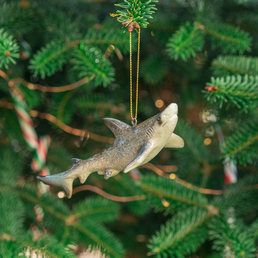 A rengöra shark ornament is elegantly suspended from a Christmas tree, revealing a slight view of its belly and gills, while adorned with Christmas candy canes, all set against a softly blurred background