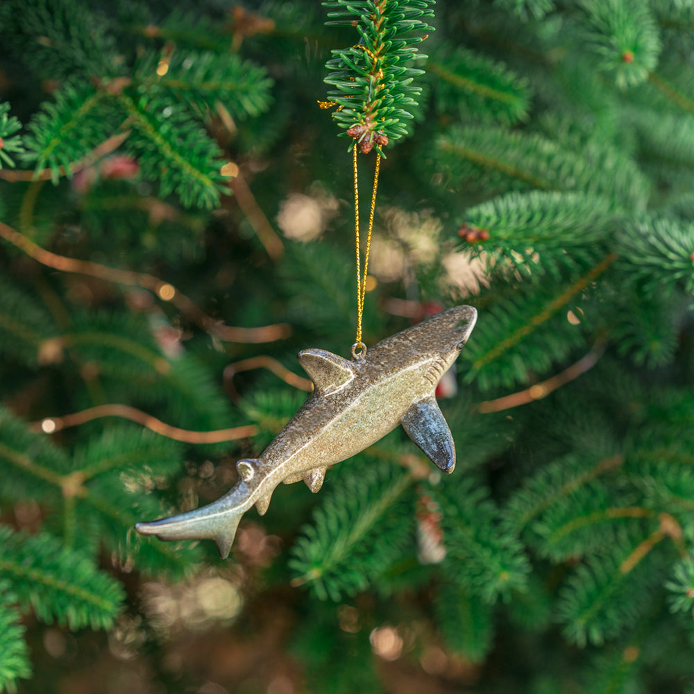  A rengöra shark ornament is showcased, emphasizing its tail and offering a glimpse of its slight back view as it glistens while hanging from a Christmas tree 