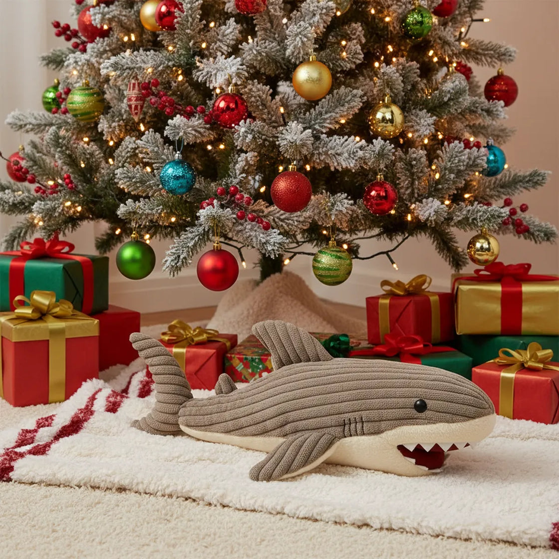Plush shark toy in front of a decorated Christmas tree with presents.
