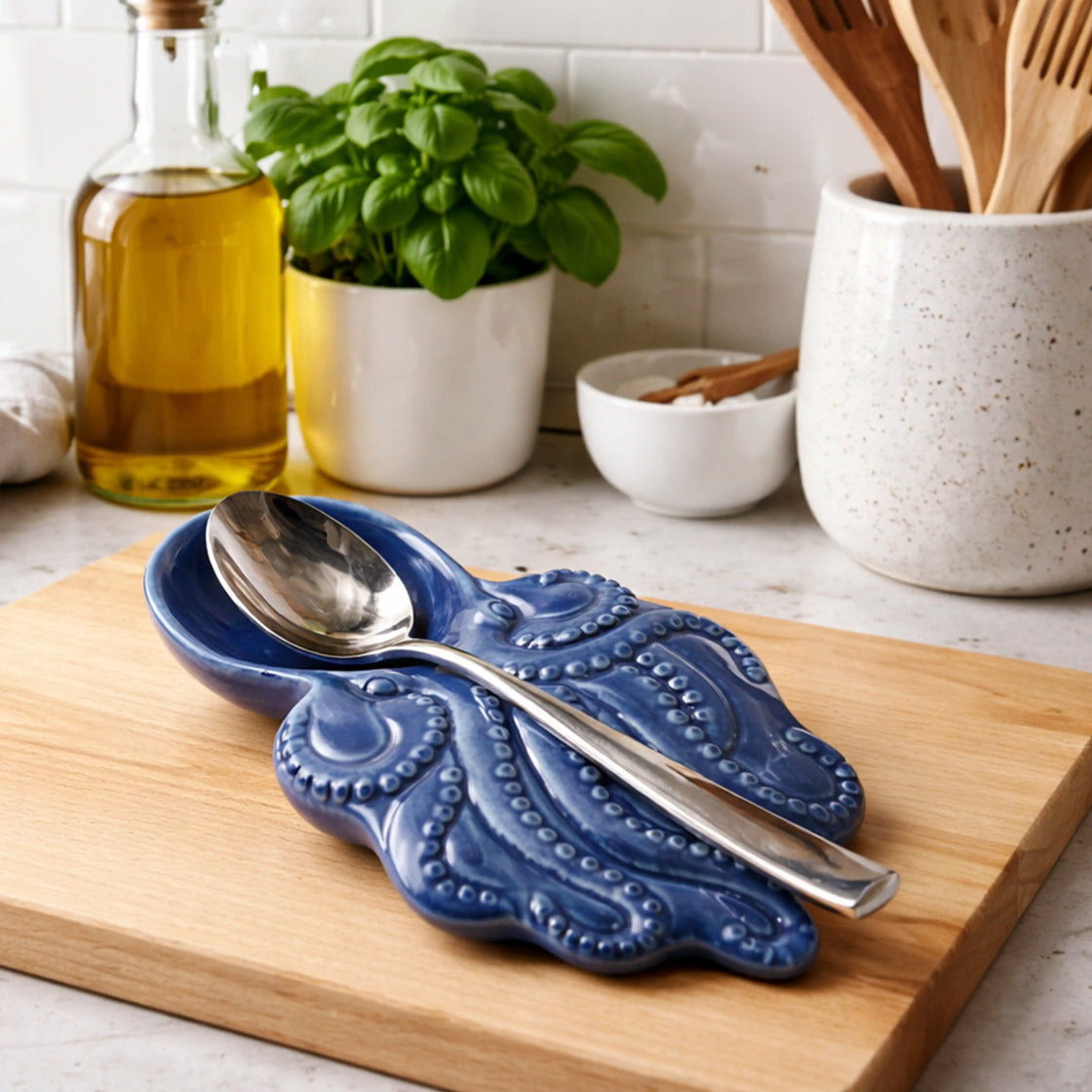 Blue ceramic spoon rest with silver spoons on a wooden cutting board in a kitchen setting.