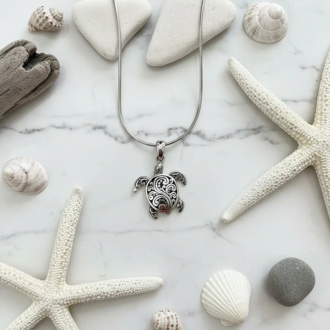 Silver turtle pendant necklace with starfish and shells on a marble surface