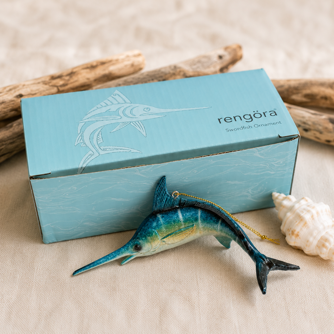 Swordfish ornament with rengöra light aqua packaging on a beige surface with driftwood and a shell.