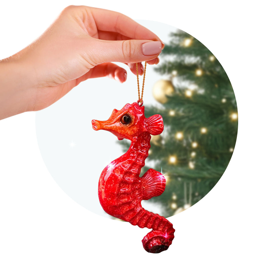 rengöra red seahorse ornament held by a hand with a golden string, against the blurred backdrop of a decorated Christmas tree