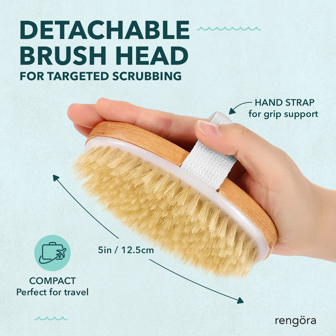 A close-up of the detachable rbamboo brush head with soft, natural bristles. A hand is holding the brush using the attached strap for a secure grip.