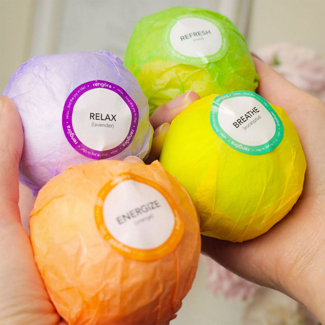 closeup of woman's hands holding 4 rengora bath bombs - Relax (lavender), Energize (orange), Refresh (mint) and Breath (eucalyptus) scents