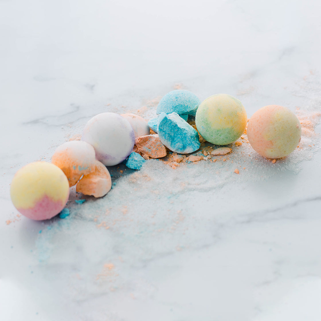 Rengora's large colorful bath bombs - some crushed and powdered - on a marble counter top