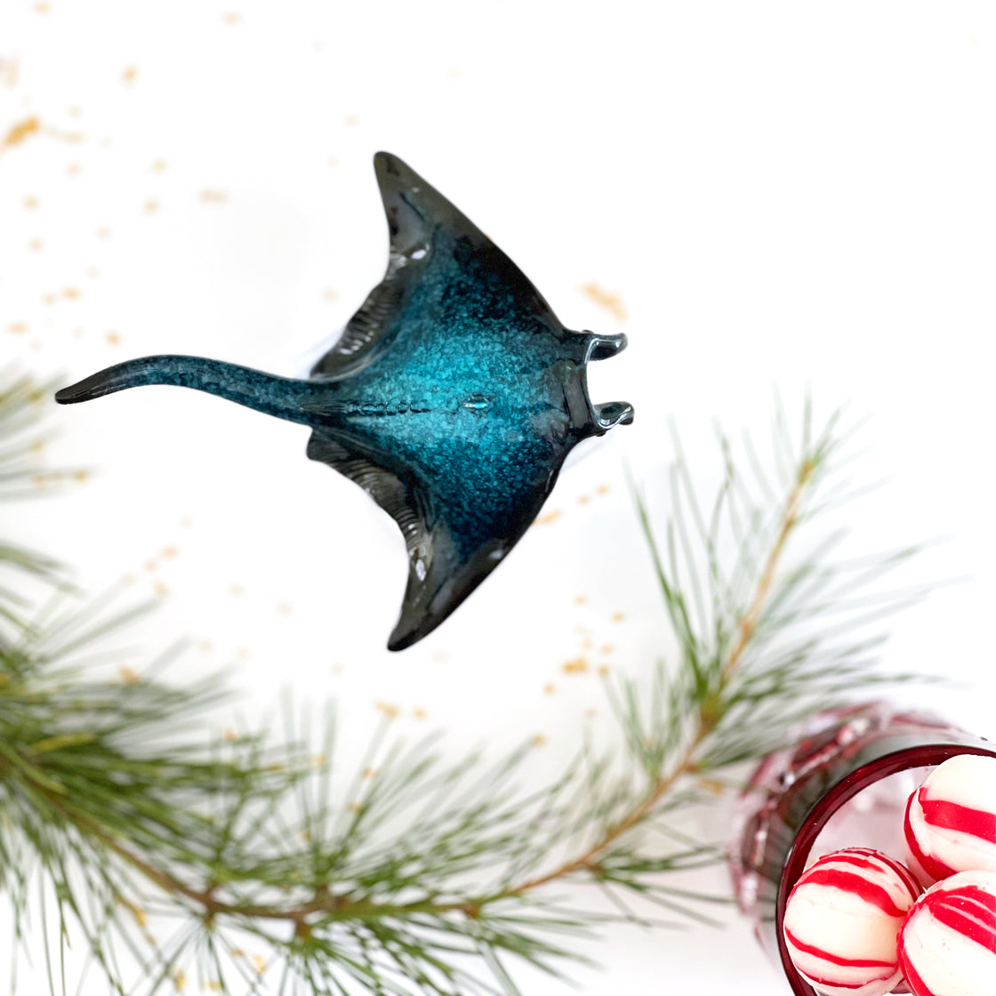 A bird's-eye perspective of the rengora manta ray Christmas ornament accompanied by pine tree leaves and a container of Christmas candies