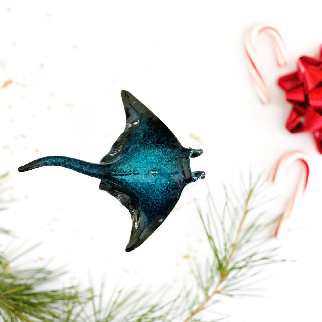 An ornament adorned with a manta ray design set against a background of pine tree leaves a festive red ribbon and Christmas candies by rengora