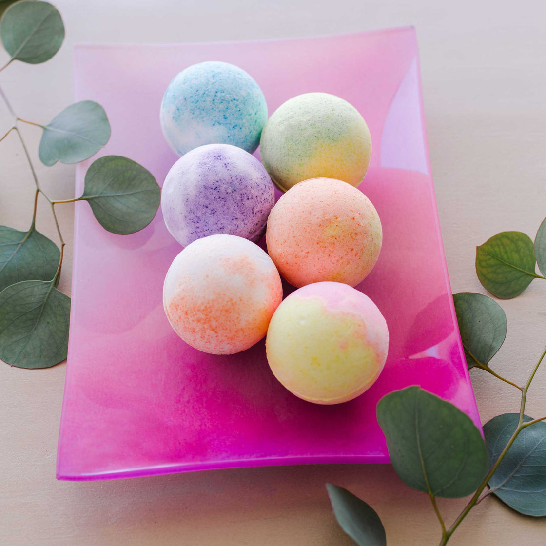 rengora's large fragrant 4oz bath bombs (6) on beautiful pink glass plate with eucalyptus leaves